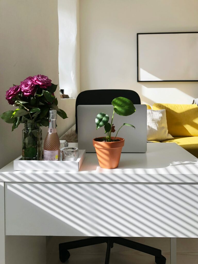 A well-lit home office with laptop, flowers, and modern decor creates a cozy work environment.